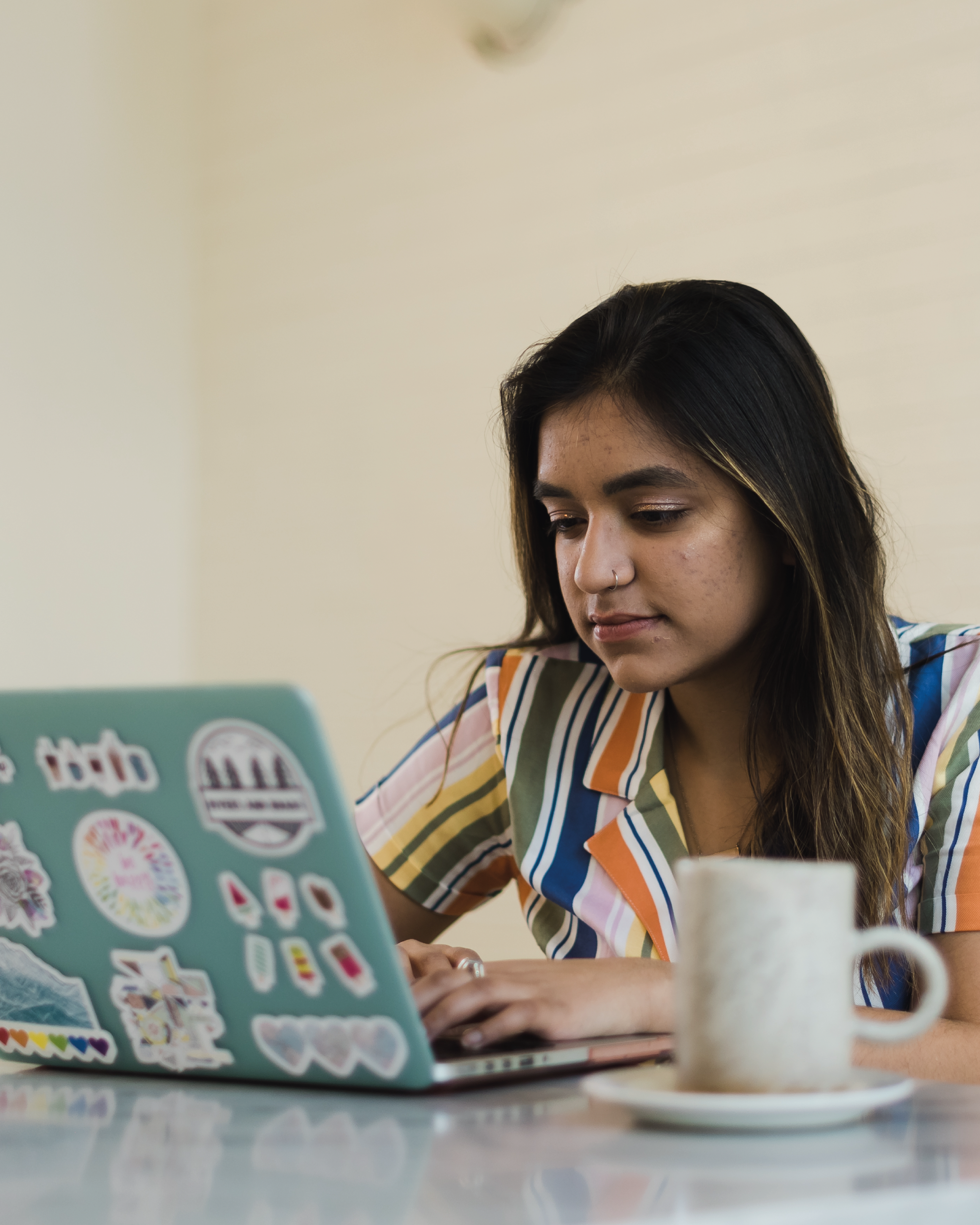 A young adult in a striped shirt on their laptop with a mug next to them